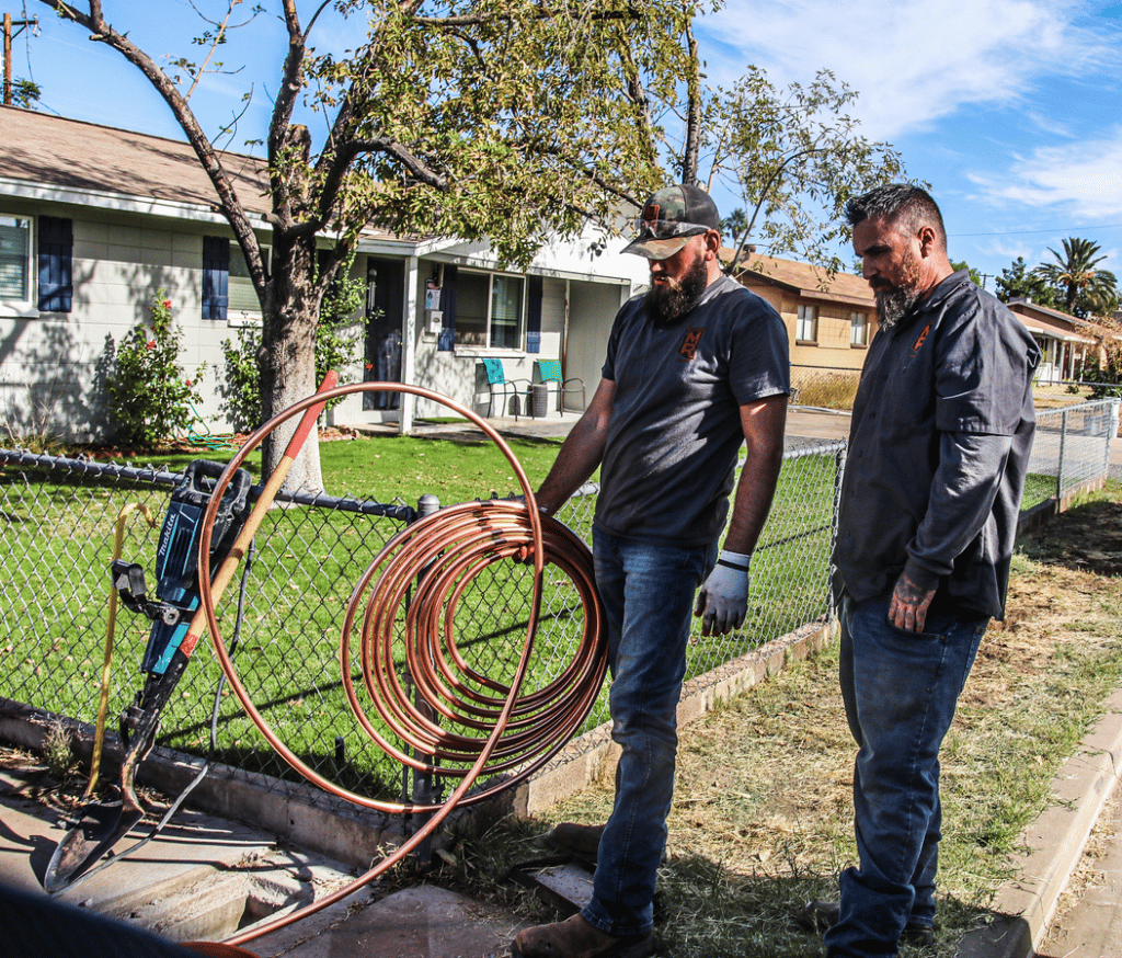 two people working with drain equipment outside of a white house with a chain fence