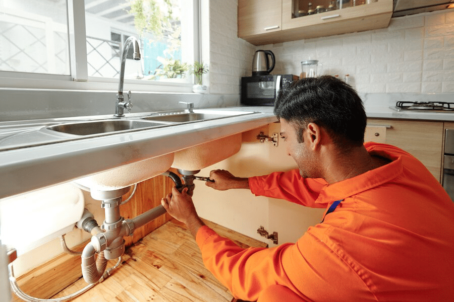 busy-young-mixed-race-plumber-orange-bodysuit-unscrewing-water-pipe-while-changing-it-sink-kitchen_274689-23811
